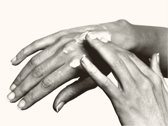 Hands applying a topical treatment. The treatment is a white cream.
